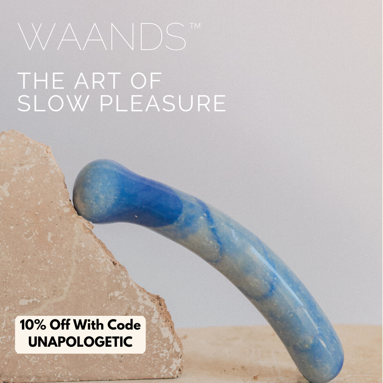 A blue crystal yoni wand with a slight curve and bulbous end leans agains tan stone with a discount code for Waands Crystal Pleasure tools with code UNAPOLOGETIC for 10% off